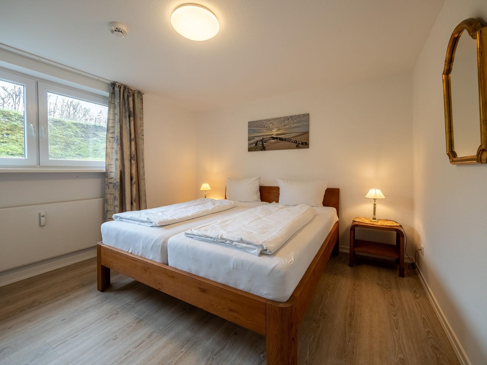 Ein Schlafzimmer mit einem Holzbett, zwei Nachttischen und einem Fenster mit Blick auf eine grüne Landschaft.