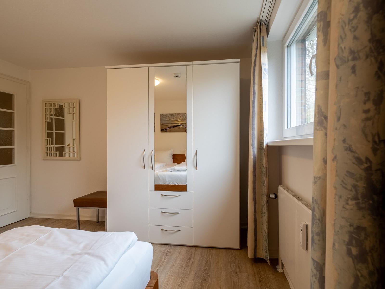 Schlafzimmer mit weißem Schrank, Fenster und Holzboden.