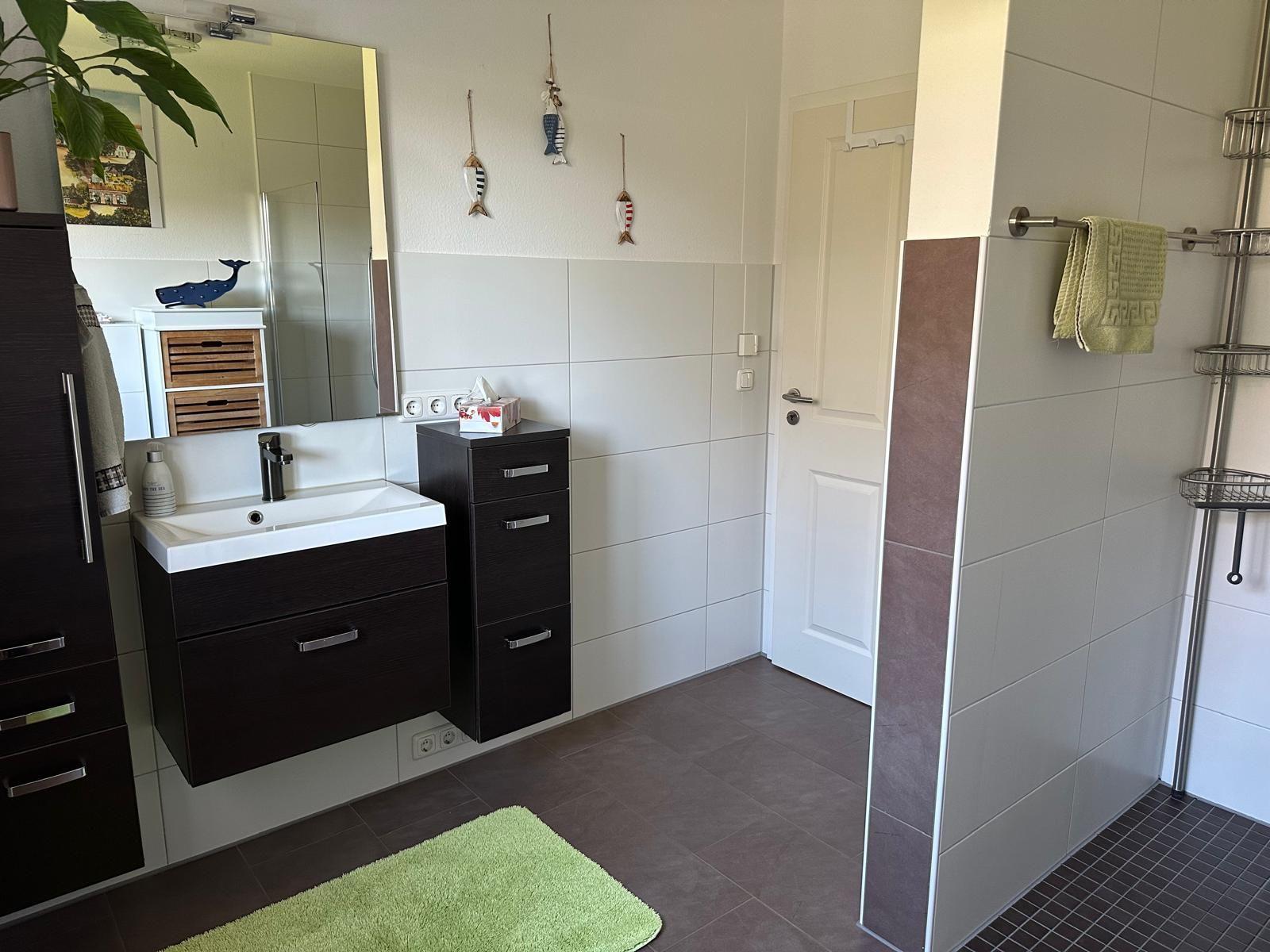Badezimmer mit Waschbecken, Spiegel und Dusche. Grün Teppich und Handtuch.