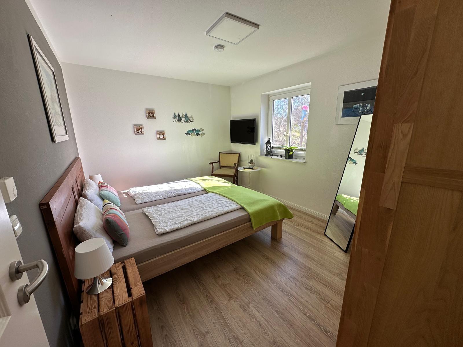 Schlafzimmer mit Bett, Fernseher und Fenster. Holzfußboden und Spiegel.