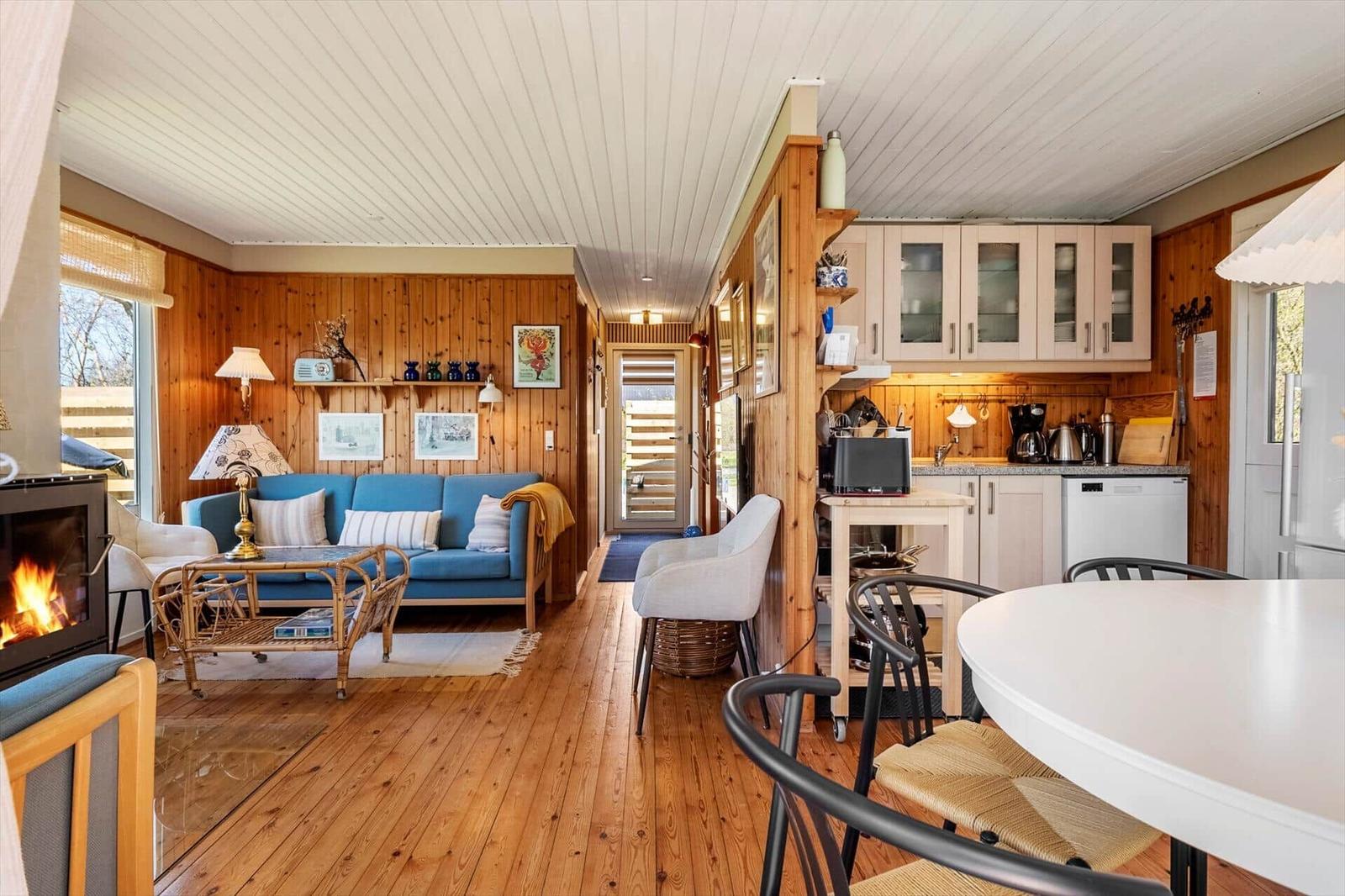 Living and kitchen area with wood wall, sofa, fireplace, and dining table.