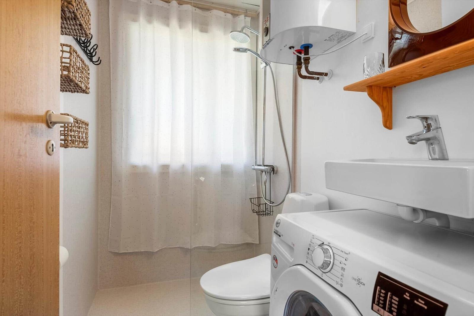Bathroom with shower, washing machine, and sink.