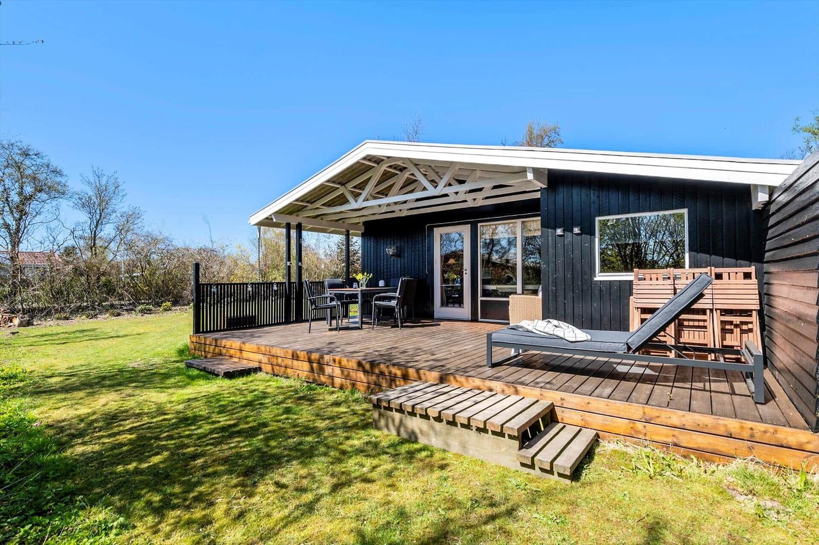 A black house with wooden terrace, sun lounger, and garden.