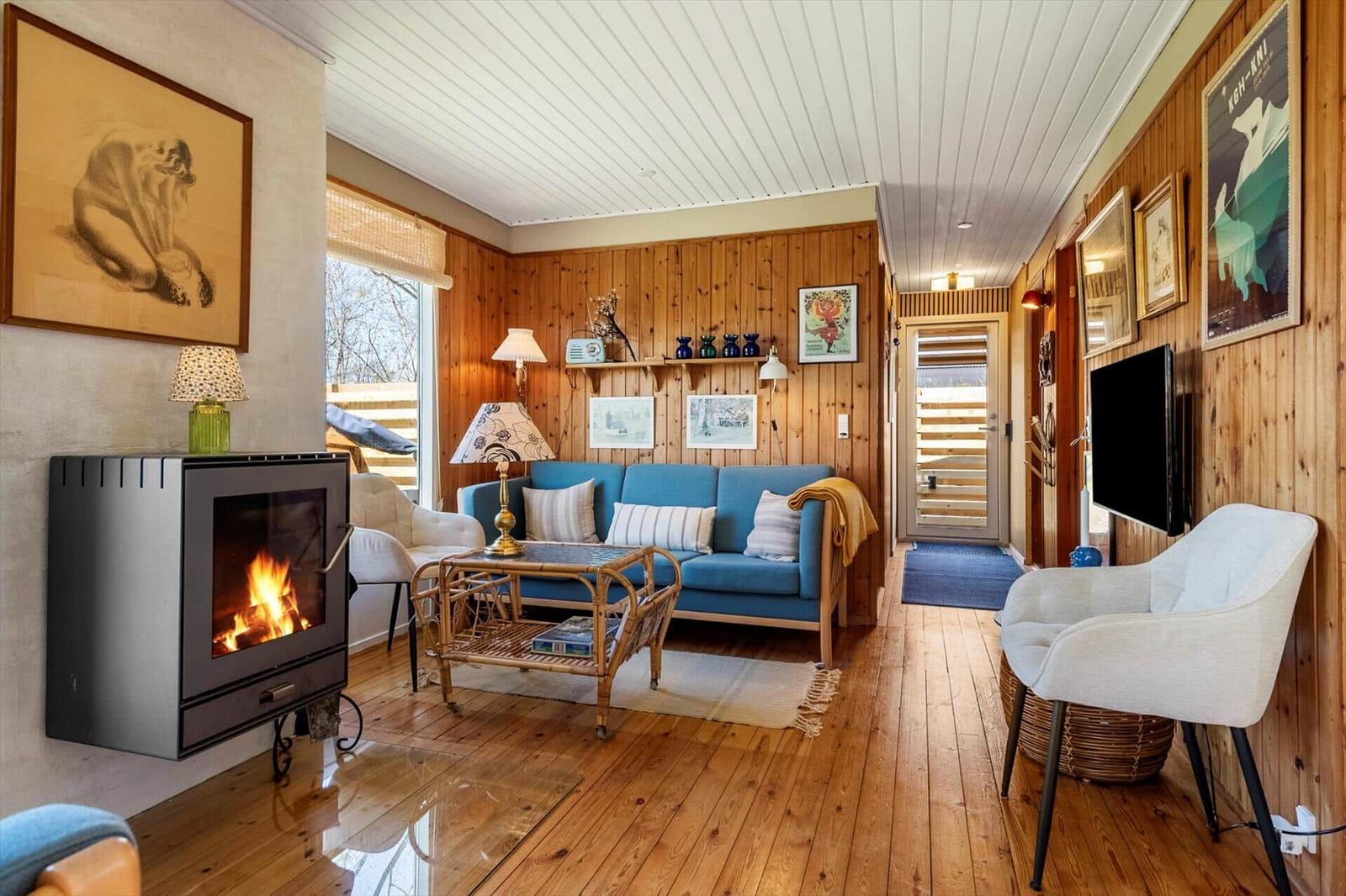 Living room with fireplace, blue sofa, and wood wall. Hallway with TV and door.