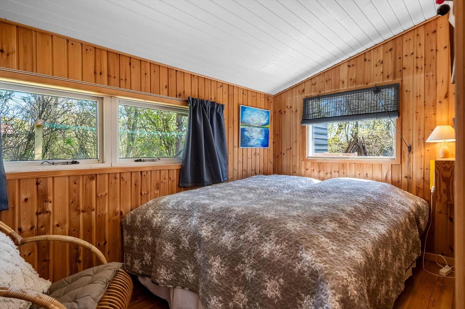 Bedroom with wooden walls, bed, and windows to the garden