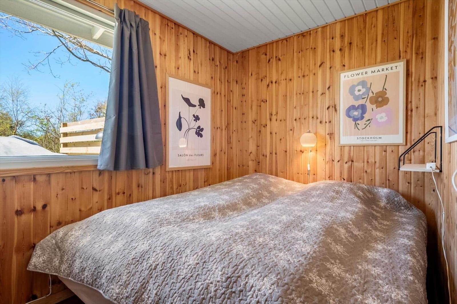Bedroom with wooden walls, bed, and window. Wall art and standing lamp.