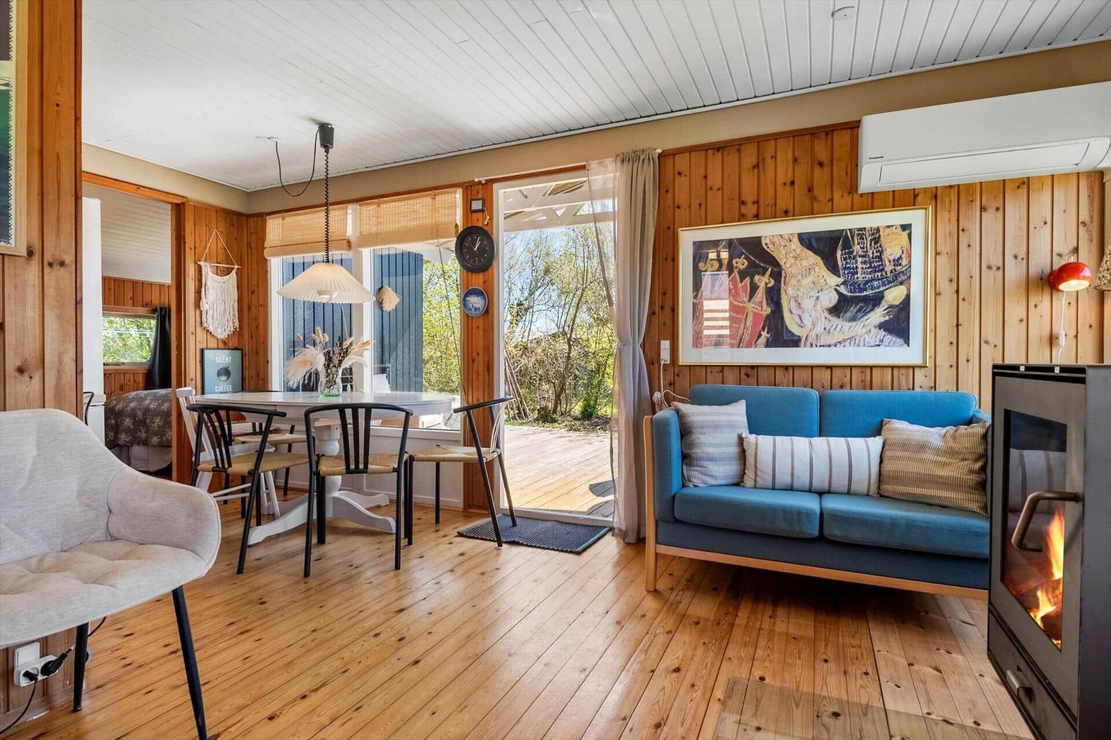 Living and dining area with wooden floors, blue sofa, and fireplace. Entrance to terrace.