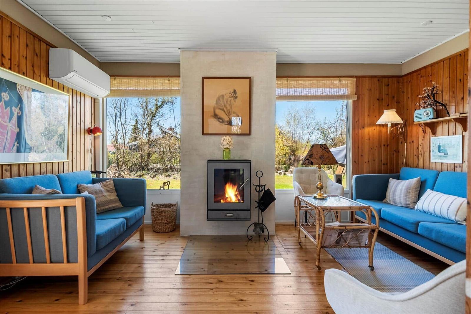 Living room with fireplace, blue sofas, and wooden walls. Garden view through windows.