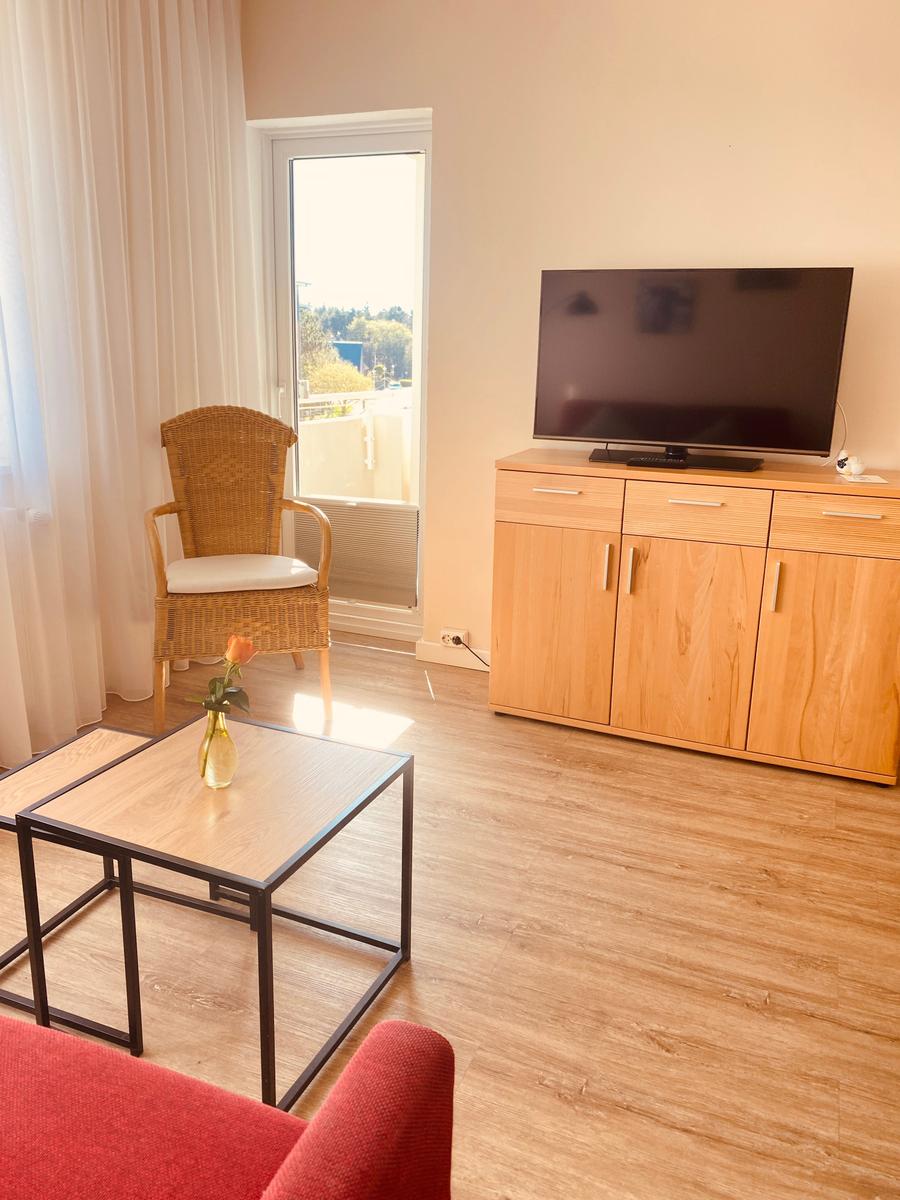 Wohnzimmer mit TV, Sitzgelegenheit und Balkontür.