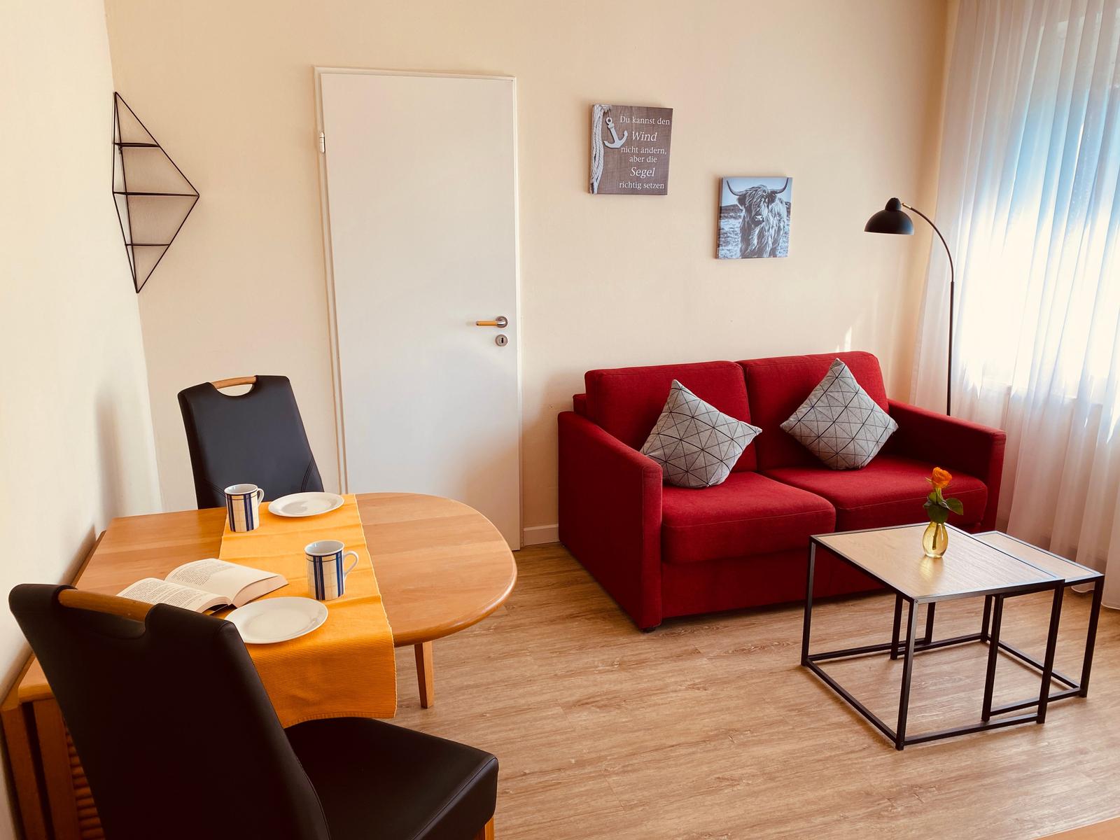 Ein Wohn- und Essbereich mit rotem Sofa, Tisch und Stühlen sowie Wandbildern.