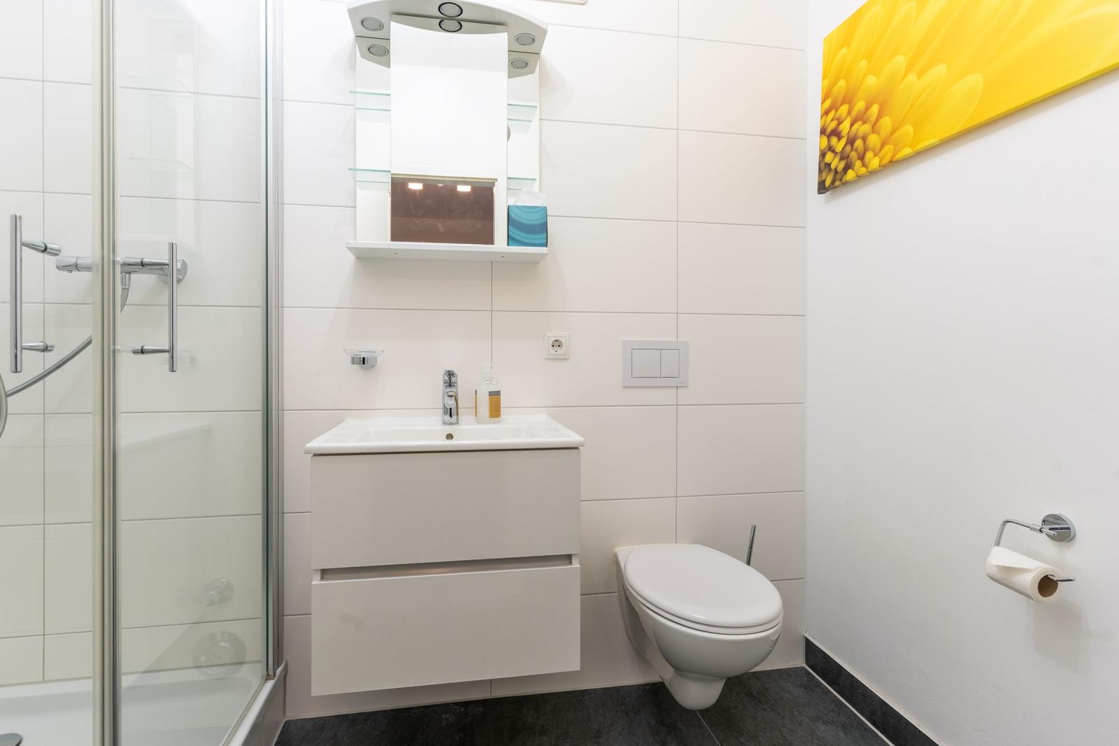 Badezimmer mit Dusche, Waschbecken und WC. Wandbild mit Sonnenblume.