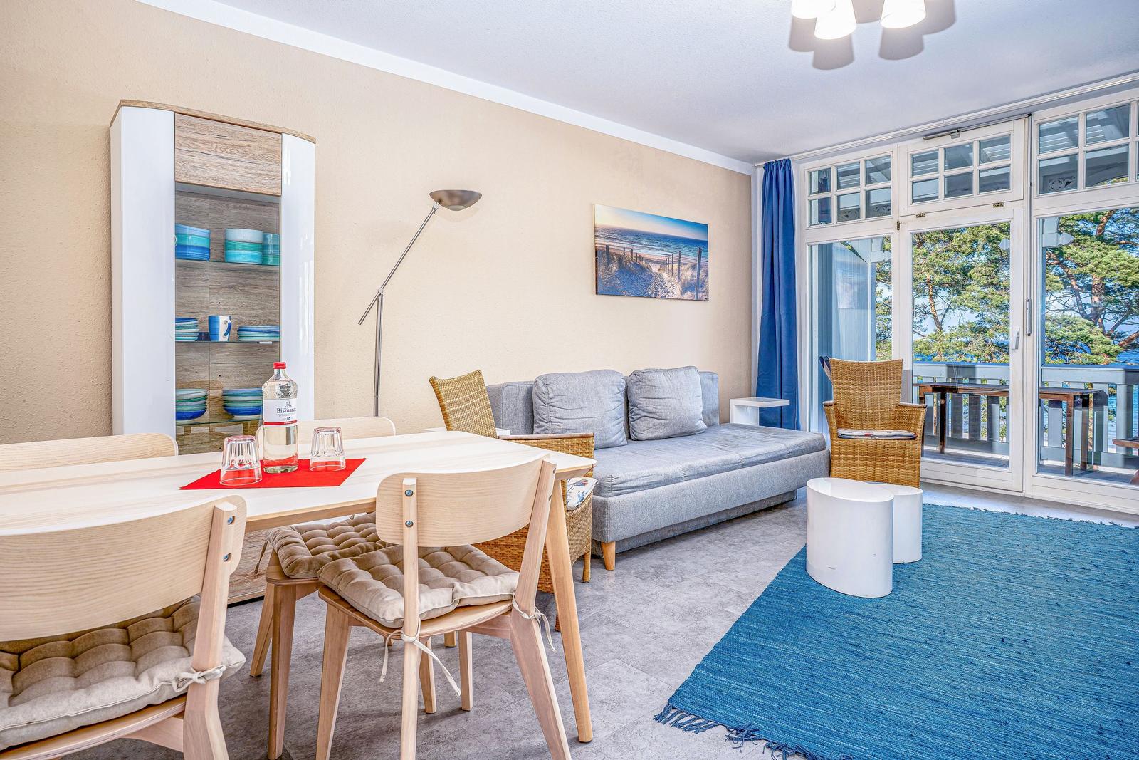 Wohn- und Essbereich mit Sofa, Tisch und Stühlen. Balkon mit Blick auf Bäume.
