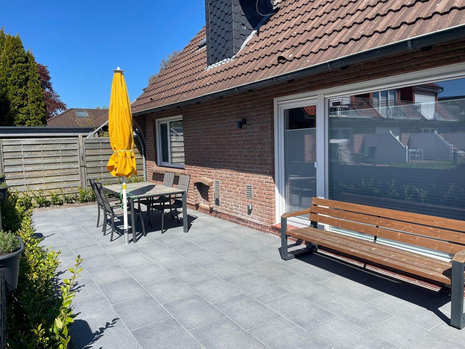 Terrasse mit Tisch, Stühlen und gelbem Sonnenschirm neben Hauswand.