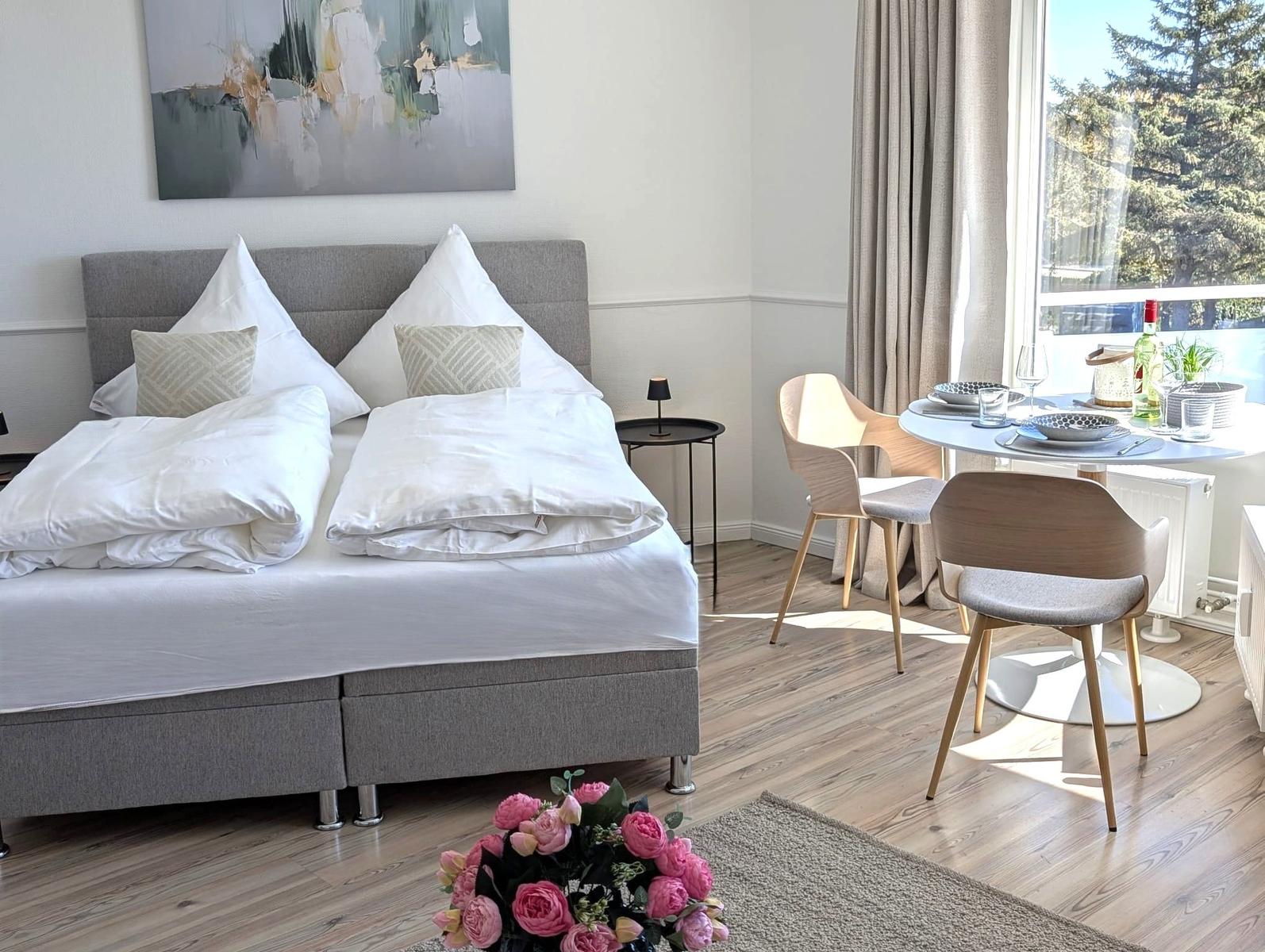 Schlafzimmer mit Doppelbett, Esstisch und Fensterblick auf Bäume