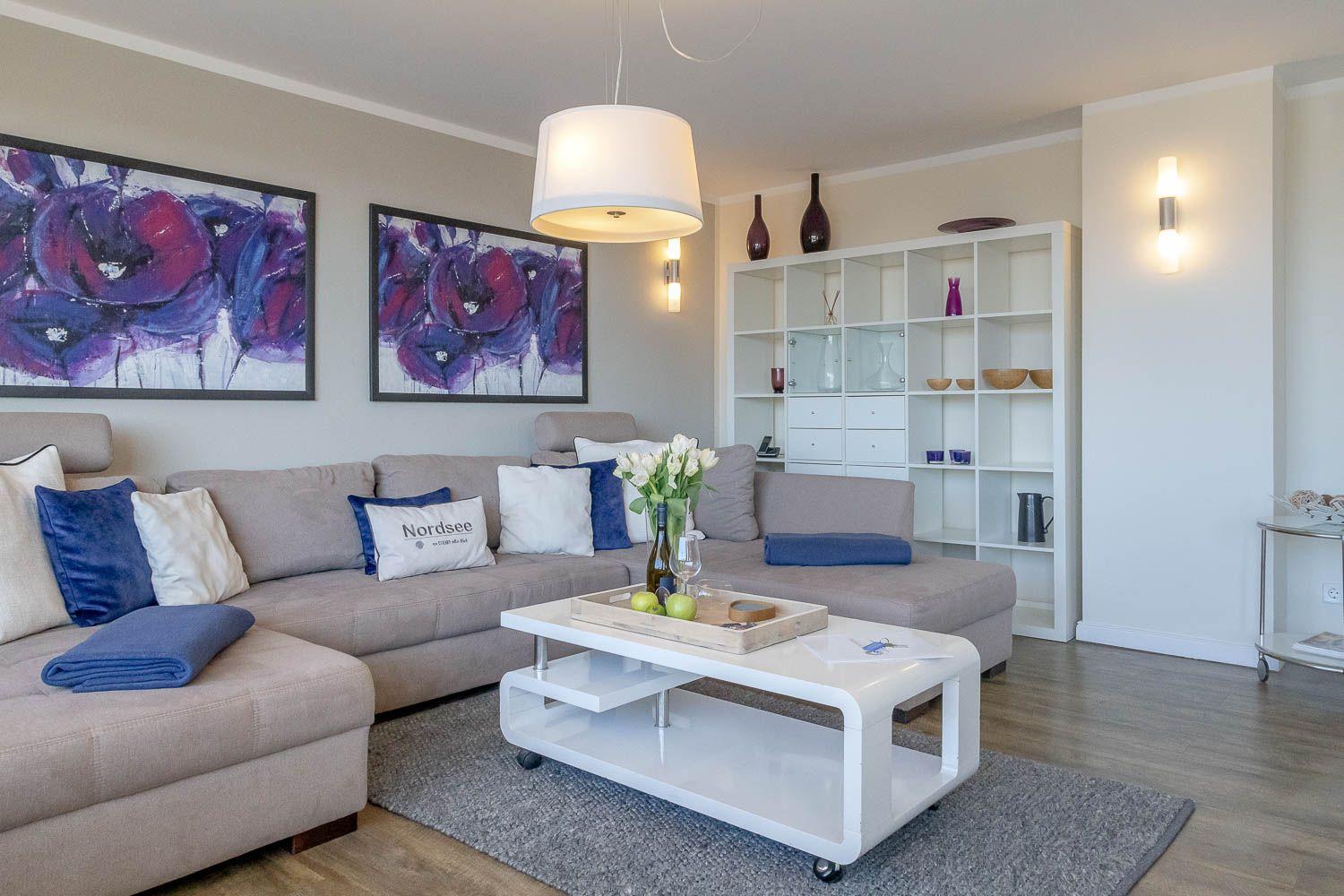 Wohnzimmer mit Sofa, Couchtisch und Wandregal. Auf der Wand hängen zwei Bilder.
