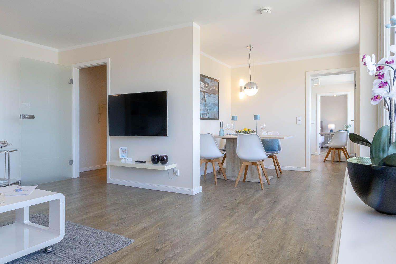 Wohn- und Essbereich mit TV, Tisch und Stühlen. Holzboden und moderne Einrichtung.