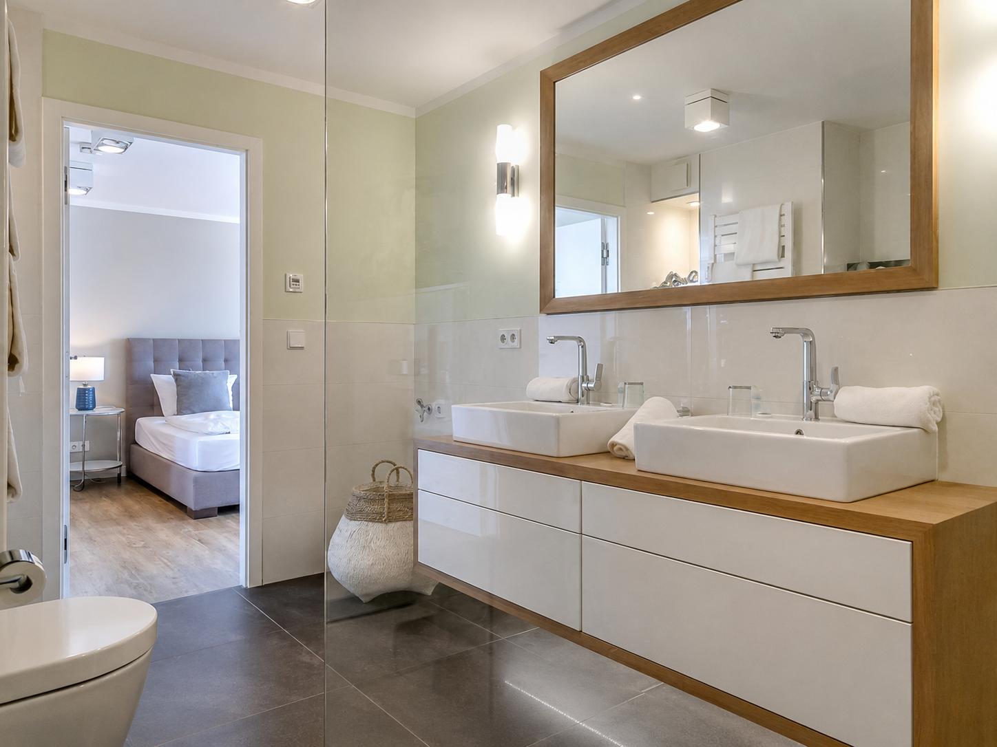 Badezimmer mit Doppelwaschbecken, Spiegel und Blick in Schlafzimmer.