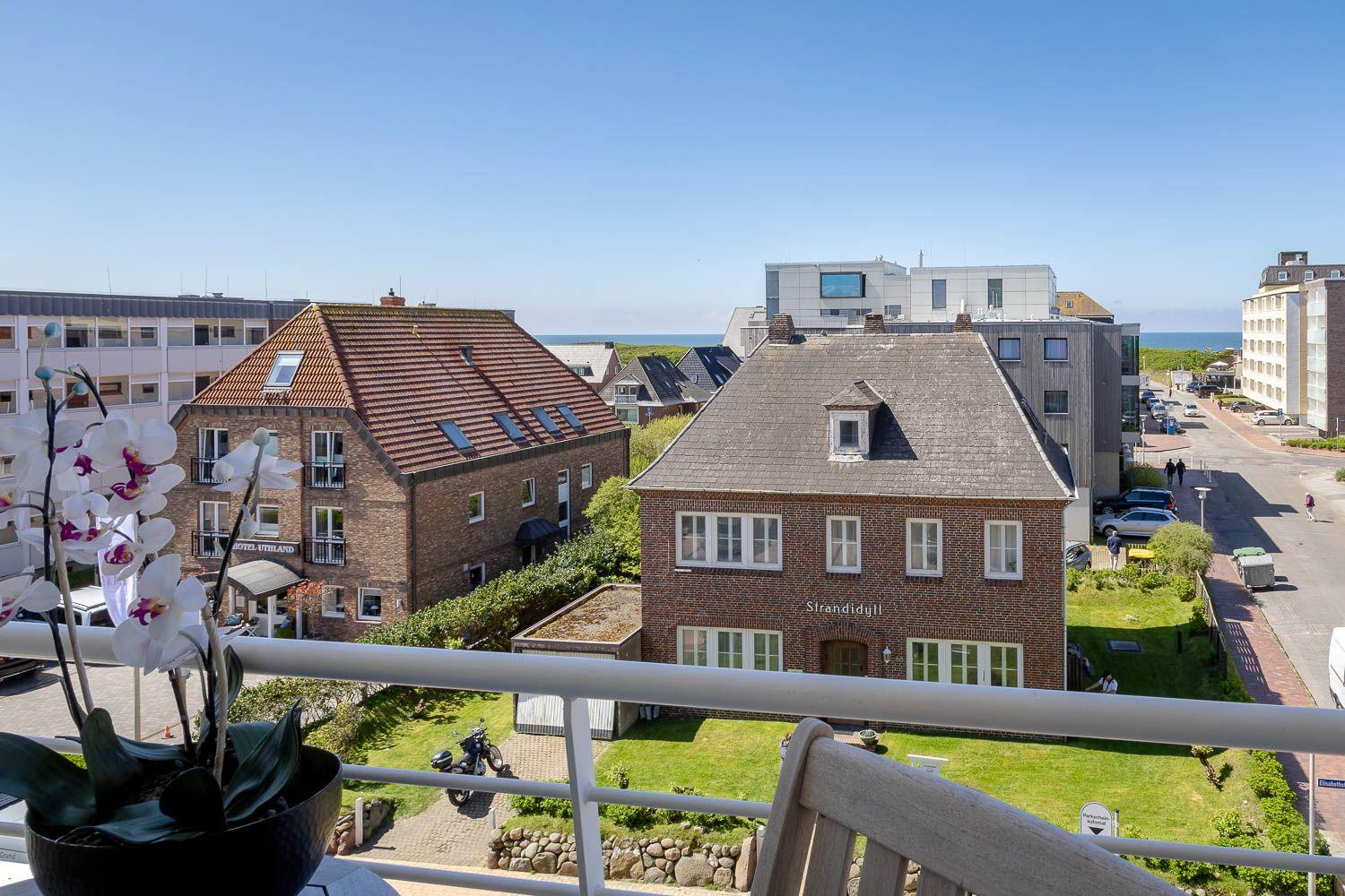 Blick von Balkon auf Straße, Häuser und Meer. Orchidee im Vordergrund.
