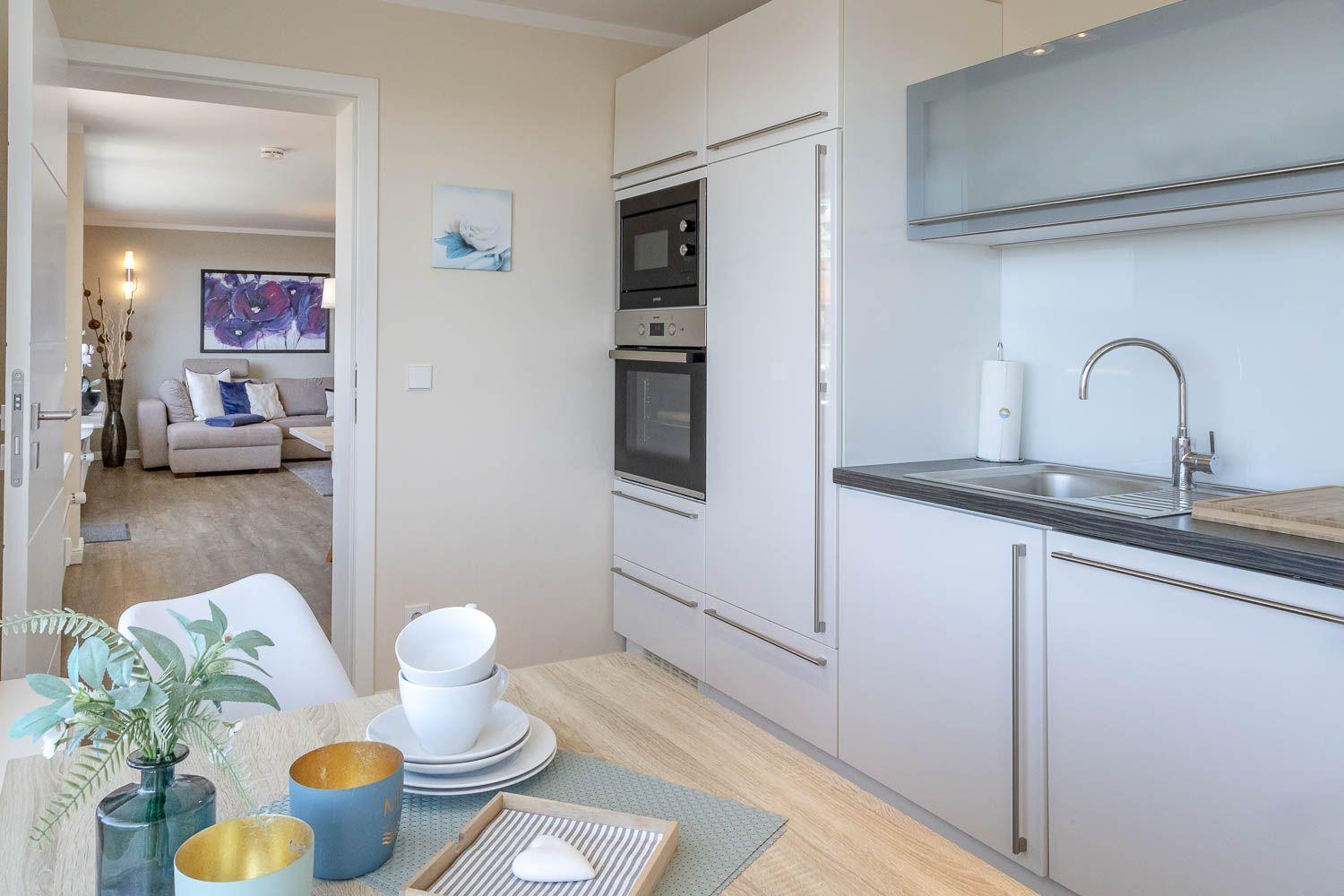 Küche mit weißen Schränken, Edelstahlspüle und Blick in Wohnzimmer.
