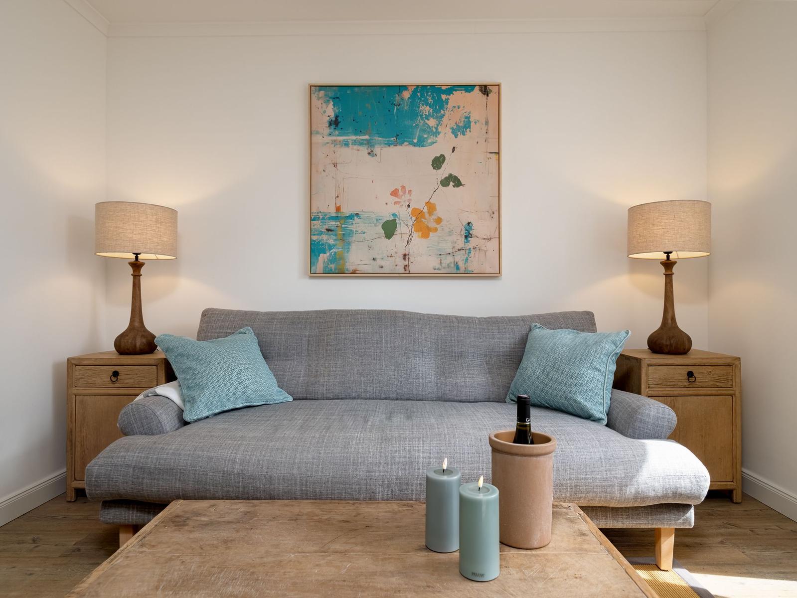 Ein grauer Sofa mit zwei Kissen, zwei Lampen und einem Bild an der Wand.
