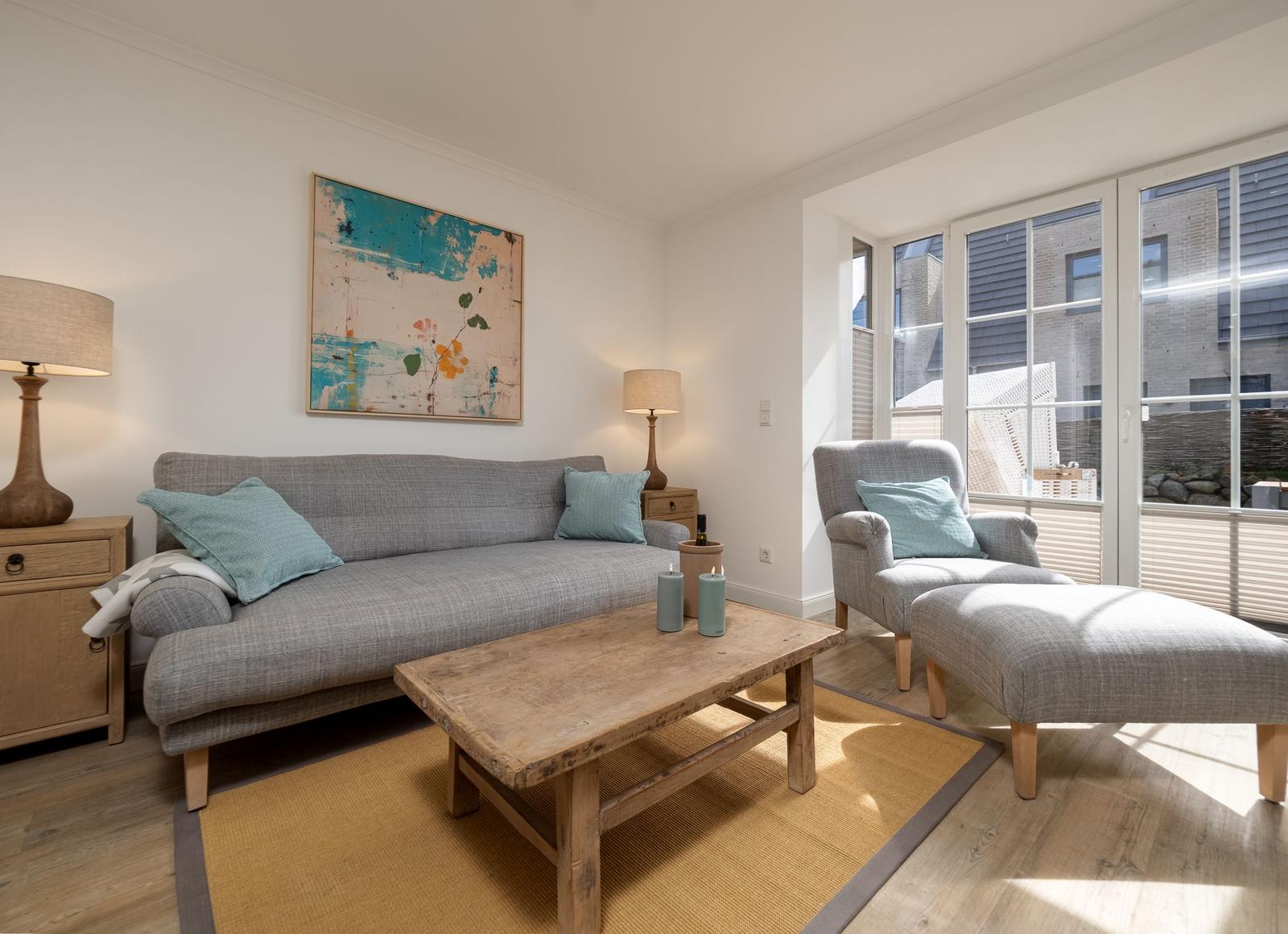 Wohnzimmer mit Sofa, Sessel und Tisch. Wandbild und große Fenster.