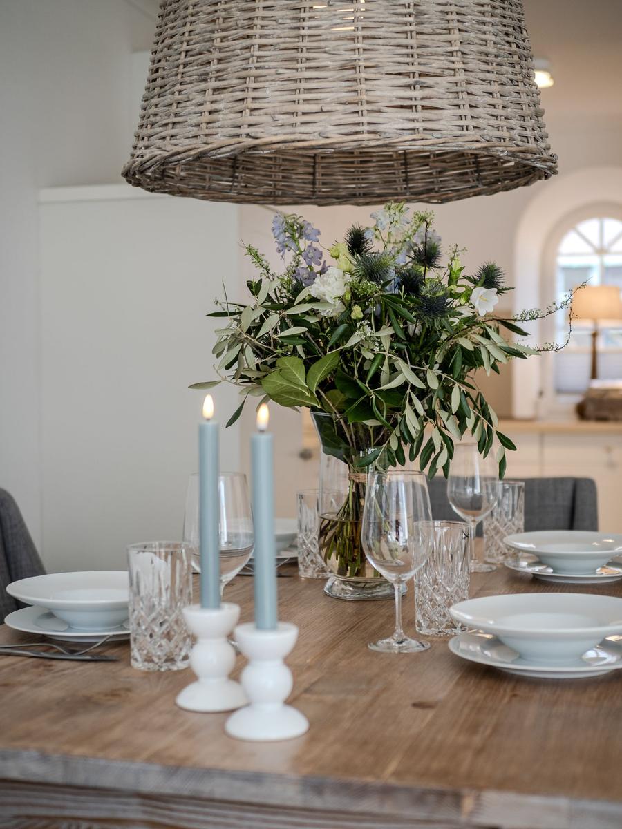 Esstisch mit Blumenvase, Kerzen und Gläsern unter einem geflochtenen Deckenlicht.