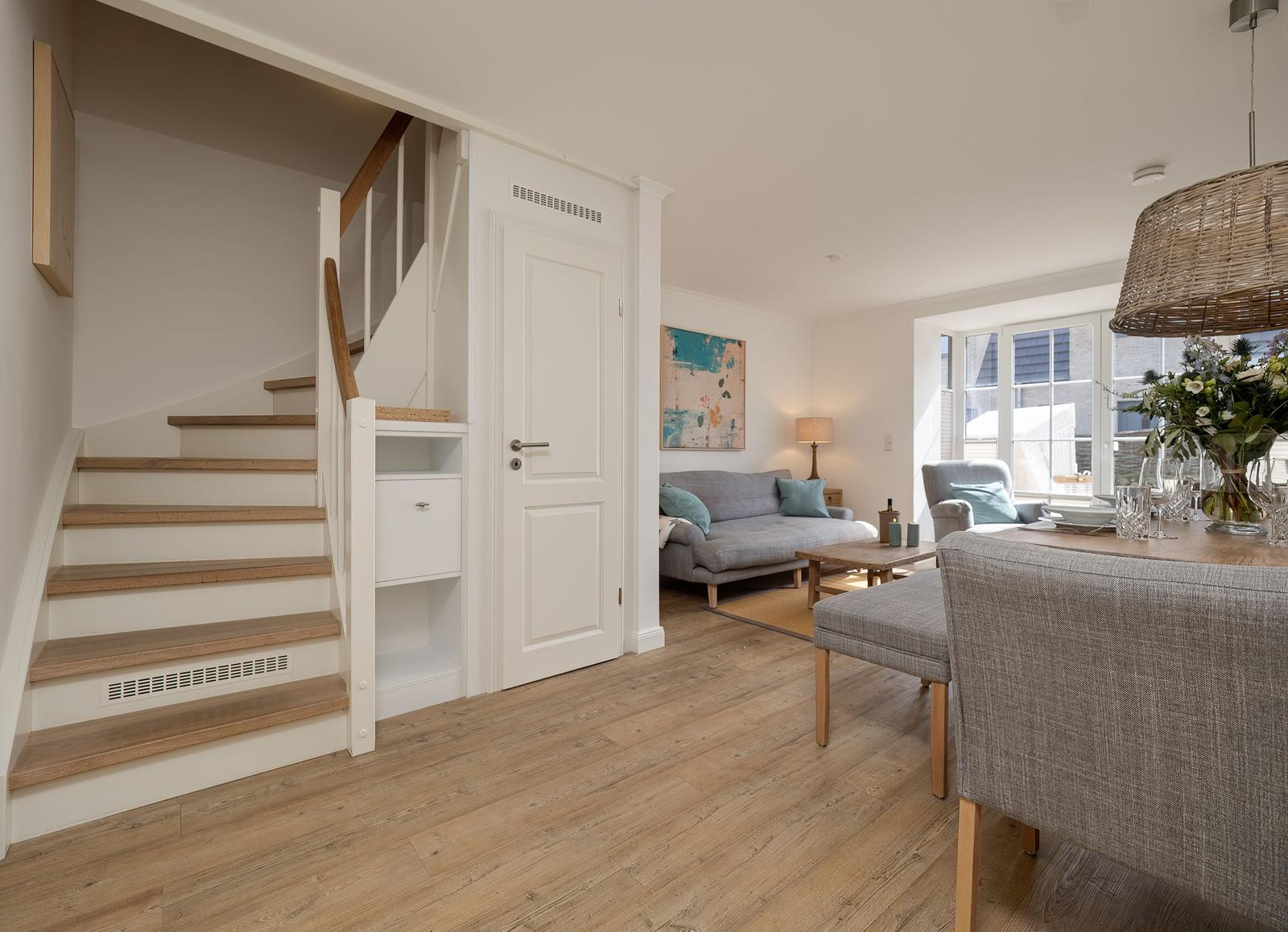 Haus mit Holzstufen, Wohnzimmer und Essbereich mit grauer Couch und Holzboden.