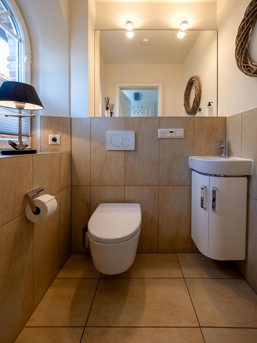 Badezimmer mit Toilette, Waschbecken und Spiegel. Holzwand und Bodenfliesen.