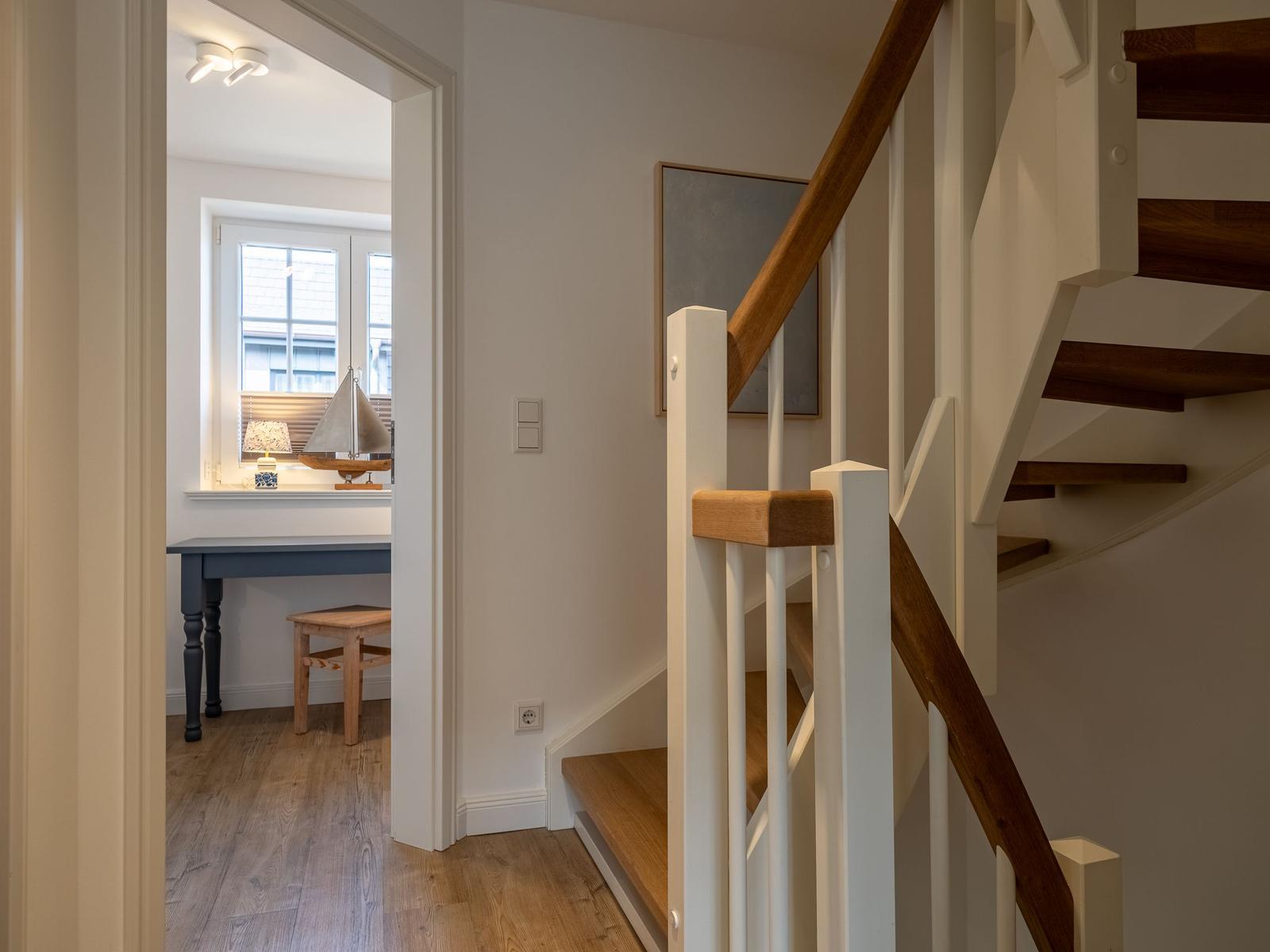 Treppenhaus mit Holzgeländer und Blick in Arbeitszimmer mit Schreibtisch.