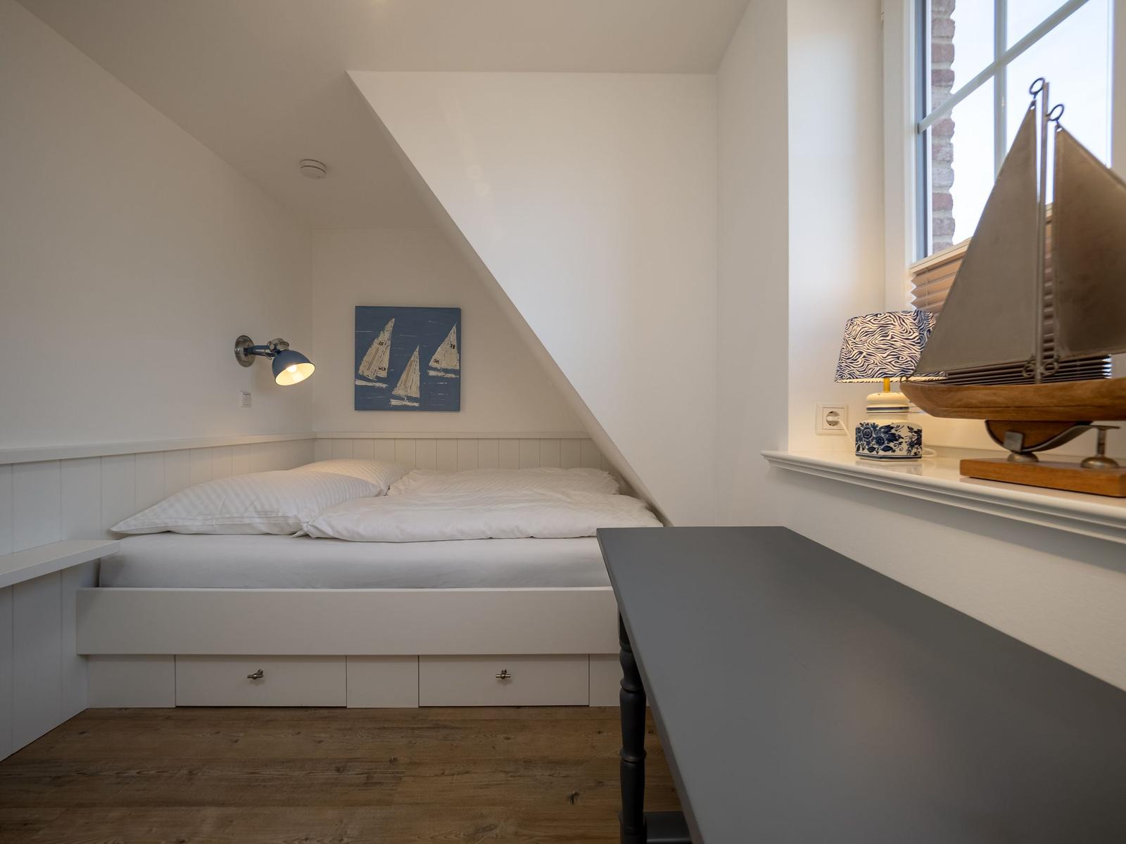 Schlafzimmer mit Dachschrägen, Bett mit Schubladen, Nachttisch und Segelbootmodell.