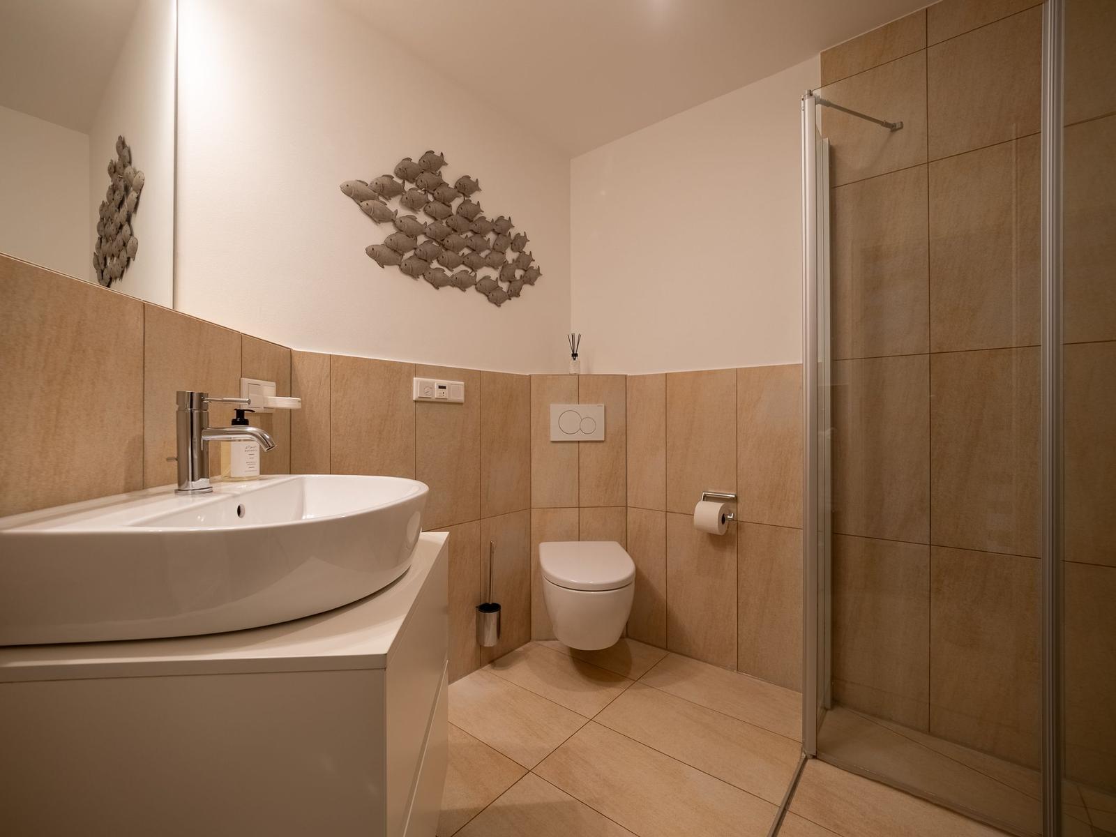 Badezimmer mit Dusche, Toilette und Waschbecken mit Wanddekoration.