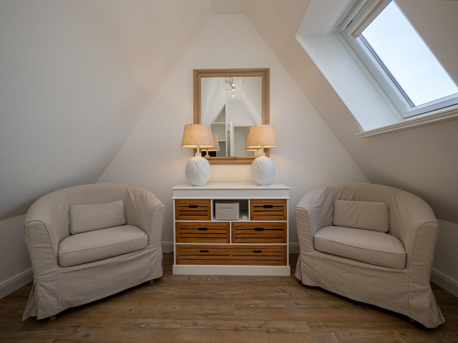 Zwei Sessel stehen vor einem Schrank mit Spiegel und Dachfenster.