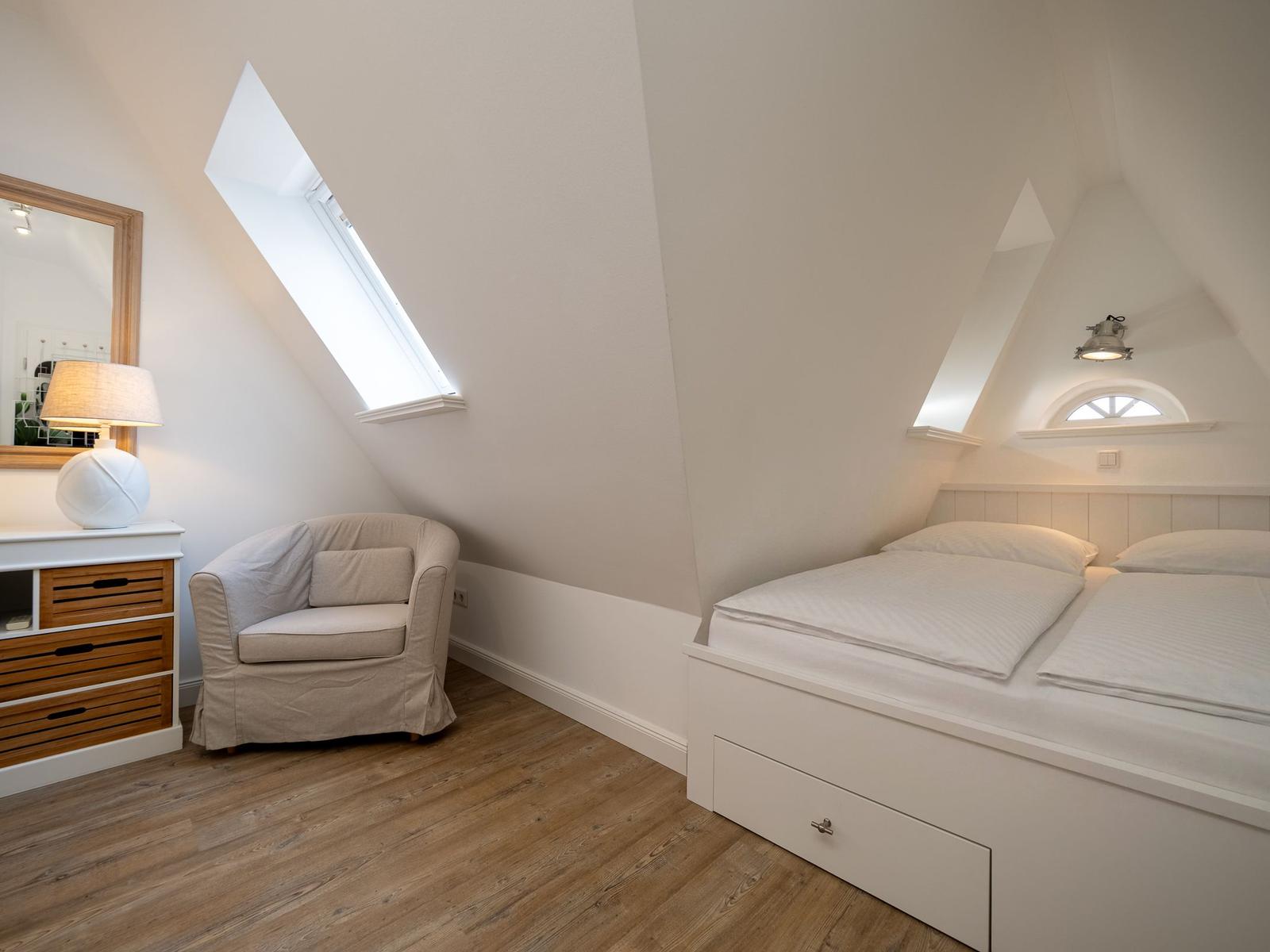 Doppelbett mit Schublade, Sessel, Schreibtisch und Dachschräge mit Fenster.