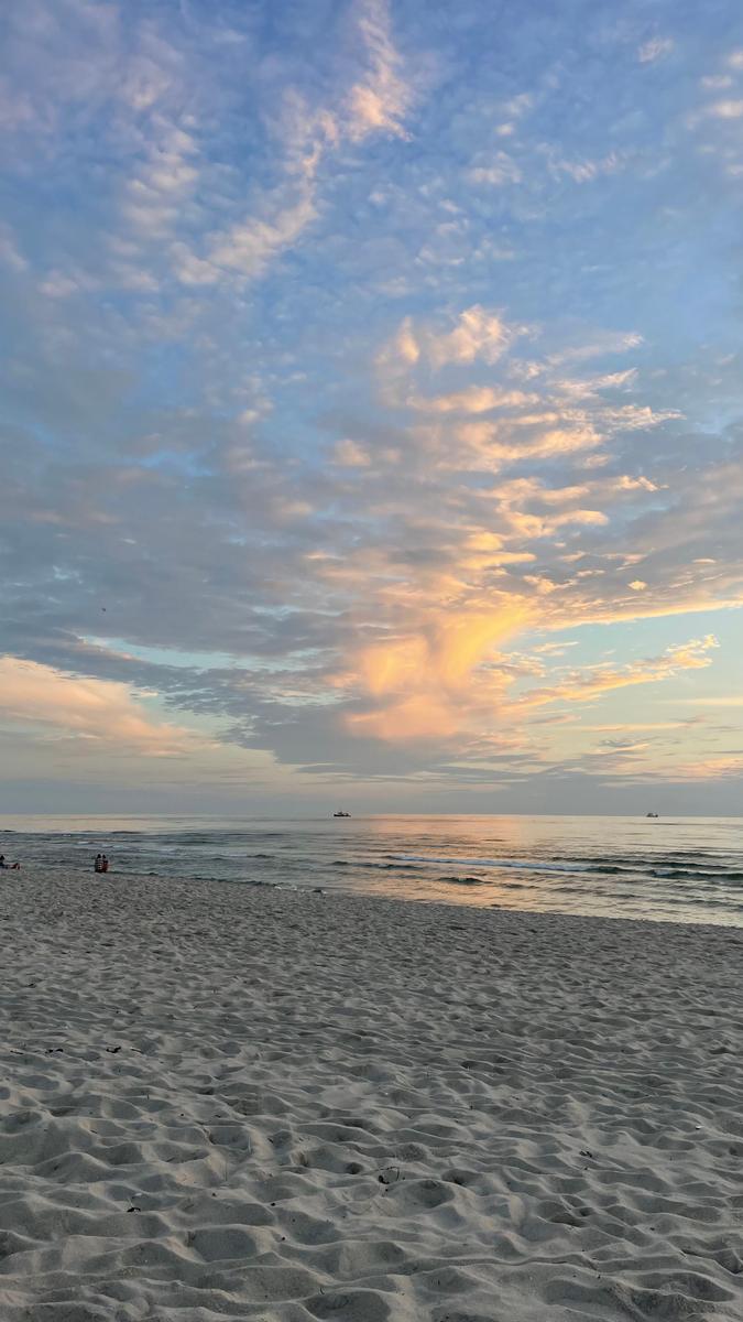 Strand bei Sonnenuntergang mit Wellen und bewölktem Himmel.