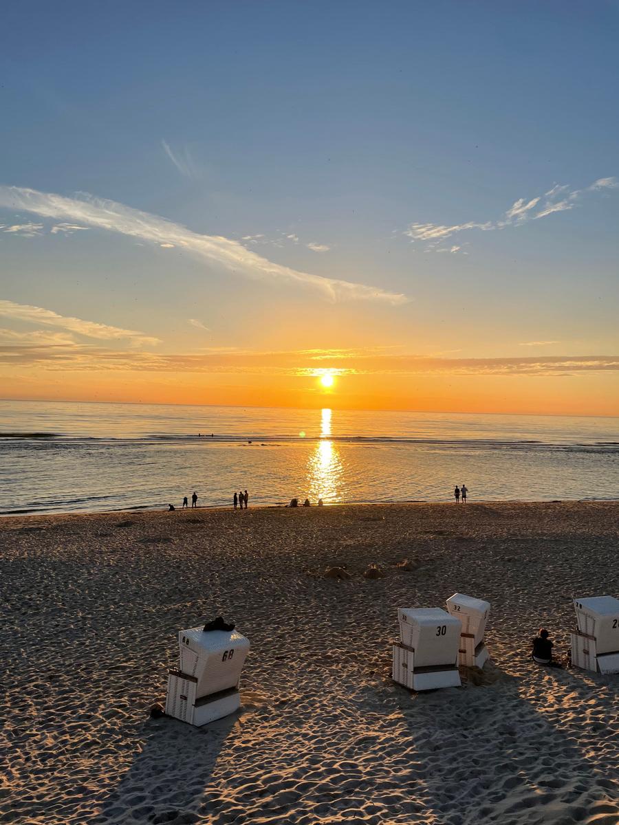 Sonnenuntergang am Strand mit Strandkörben und Menschen in der Ferne.