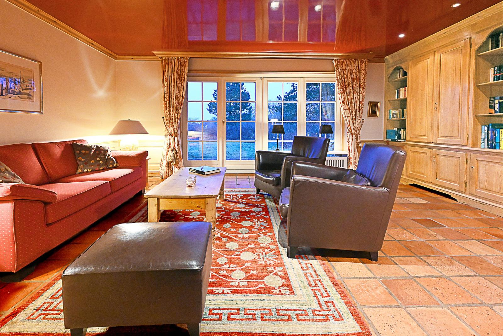 Wohnzimmer mit Sofa, Sesseln, Tisch und Teppich. Holzfußboden und Bücherregal.