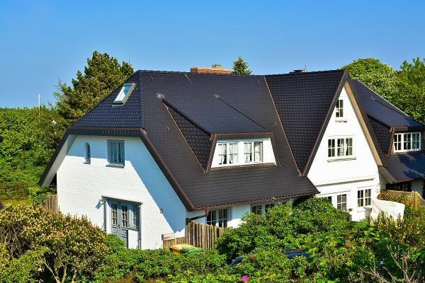 Ein weißes Haus mit dunklem Dach und mehreren Fenstern in grüner Umgebung.