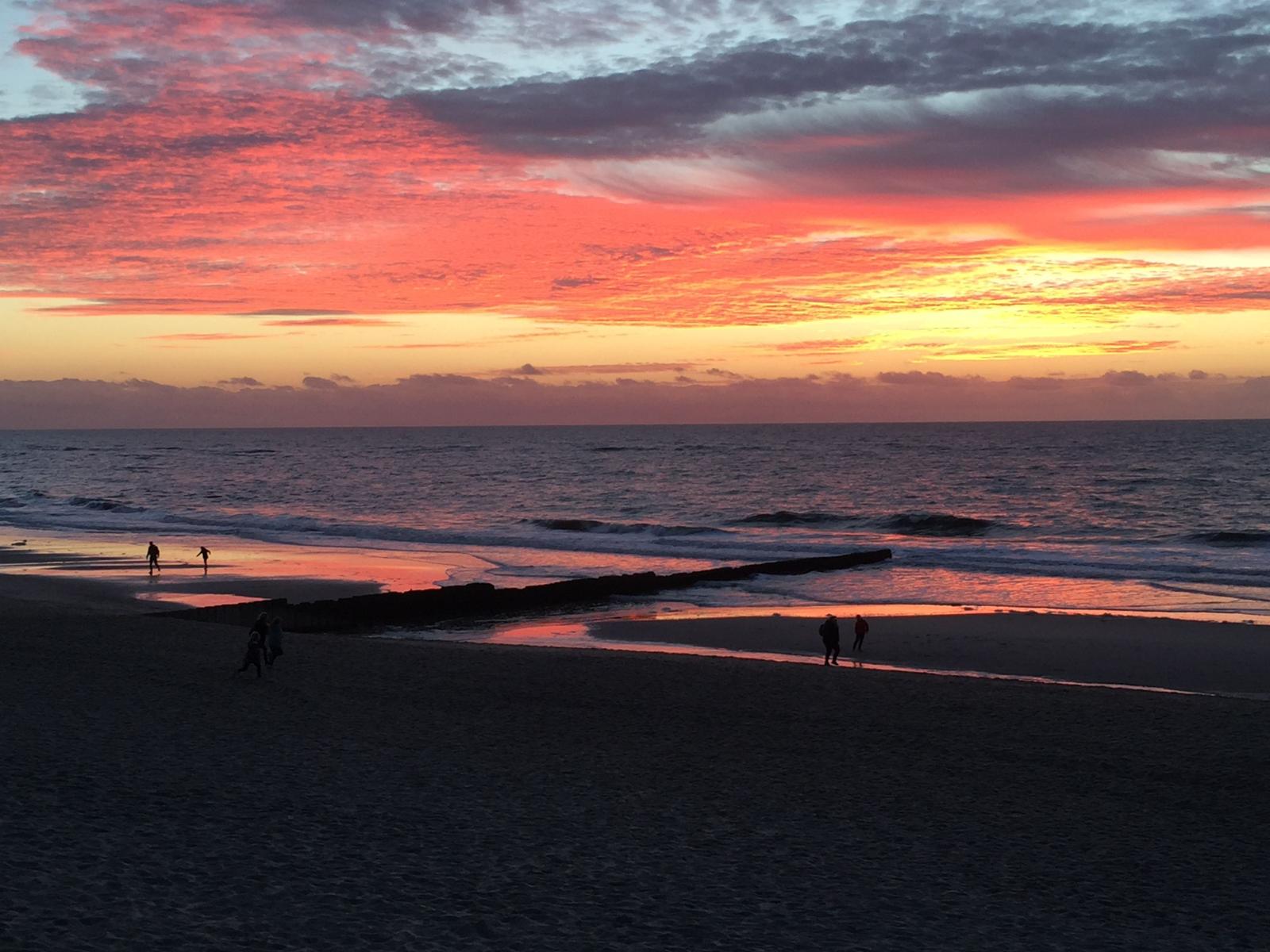 Sonnenuntergang am Strand mit Reflexion im Wasser und Silhouetten von Personen.