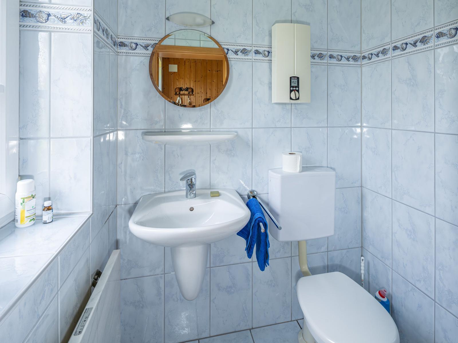 Badezimmer mit Waschbecken, Spiegel und Toilette. Wandfliesen mit Muster.
