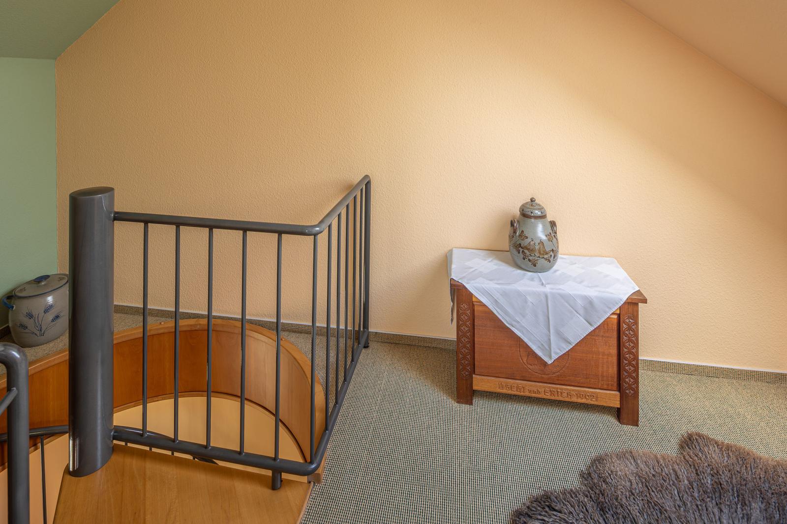 Treppenhaus mit Holzstufen, Metallgeländer und Holzschrank mit Tischdecke.