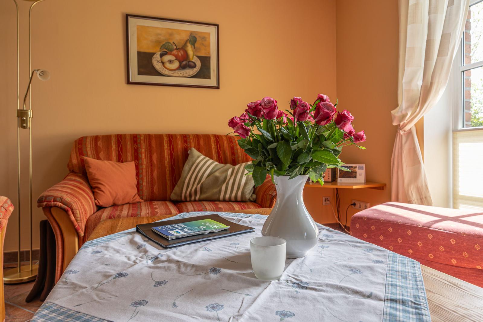 Ein Wohnzimmer mit Sofa, Tisch, Blumen und Fenster.