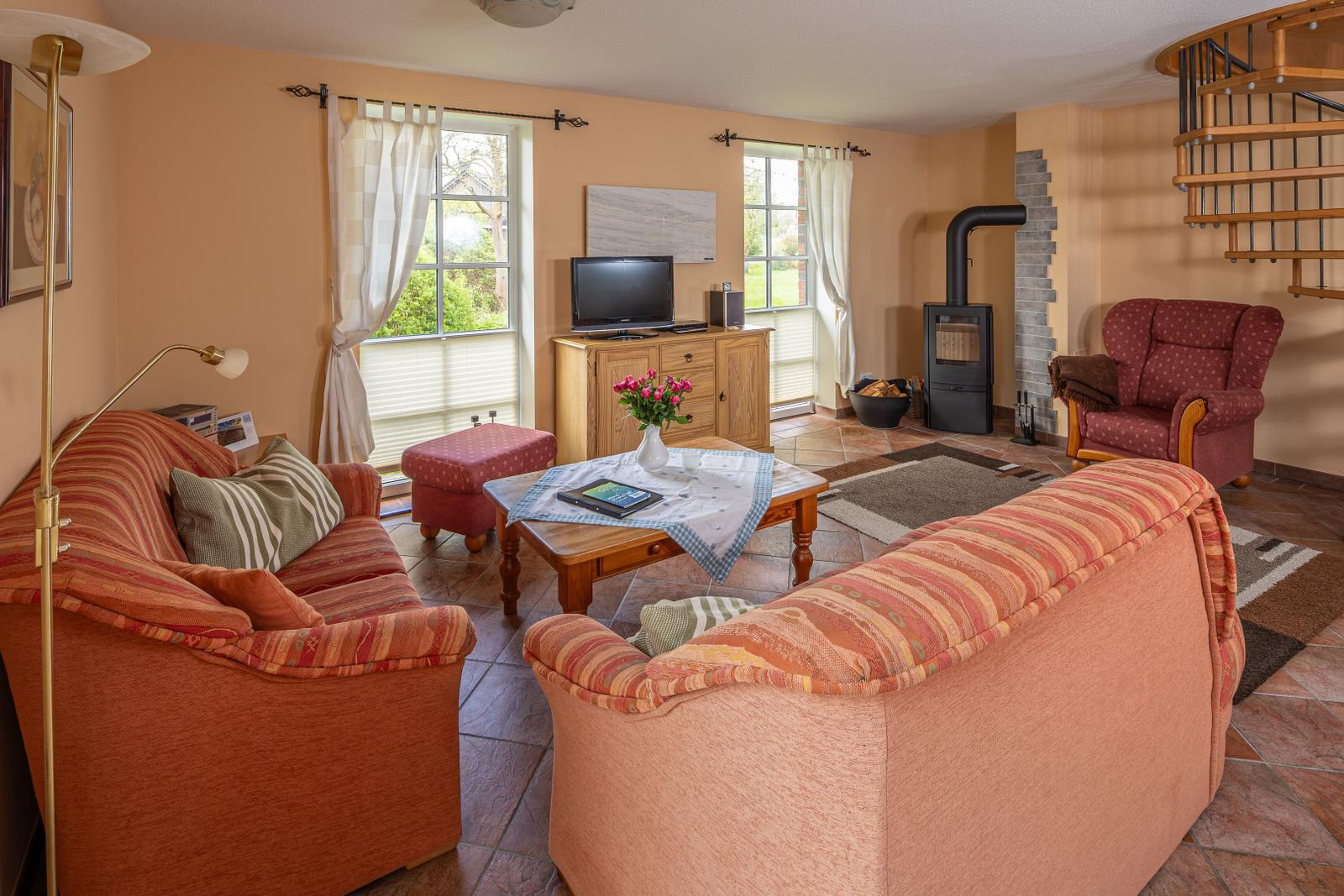 Wohnzimmer mit Sofa, Sessel, Kamin und TV. Fenster mit Blick auf Garten.