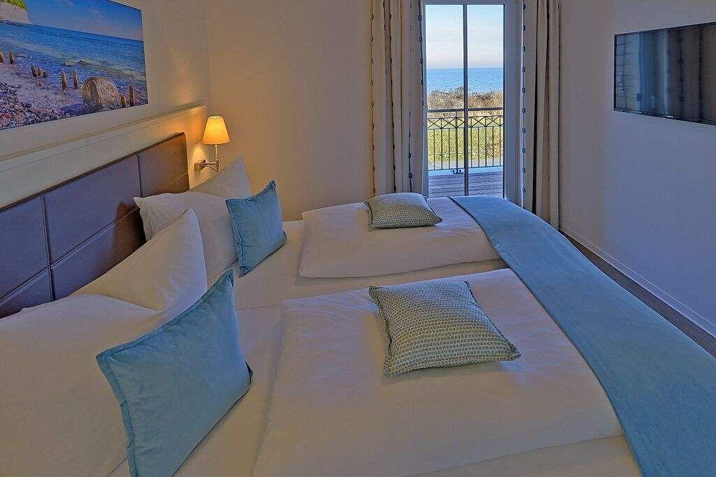 Wohnzimmer mit Sofa, Sessel und TV. Große Fensterfront mit Blick.