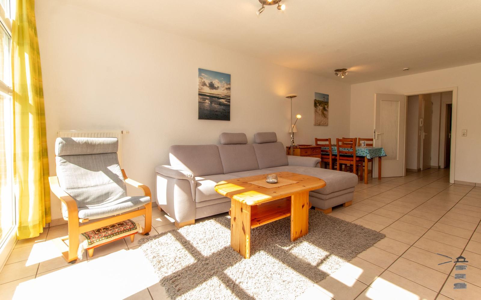 Wohnzimmer mit Sofa, Sessel und Esstisch. Gelbe Vorhänge und Holzmöbel.