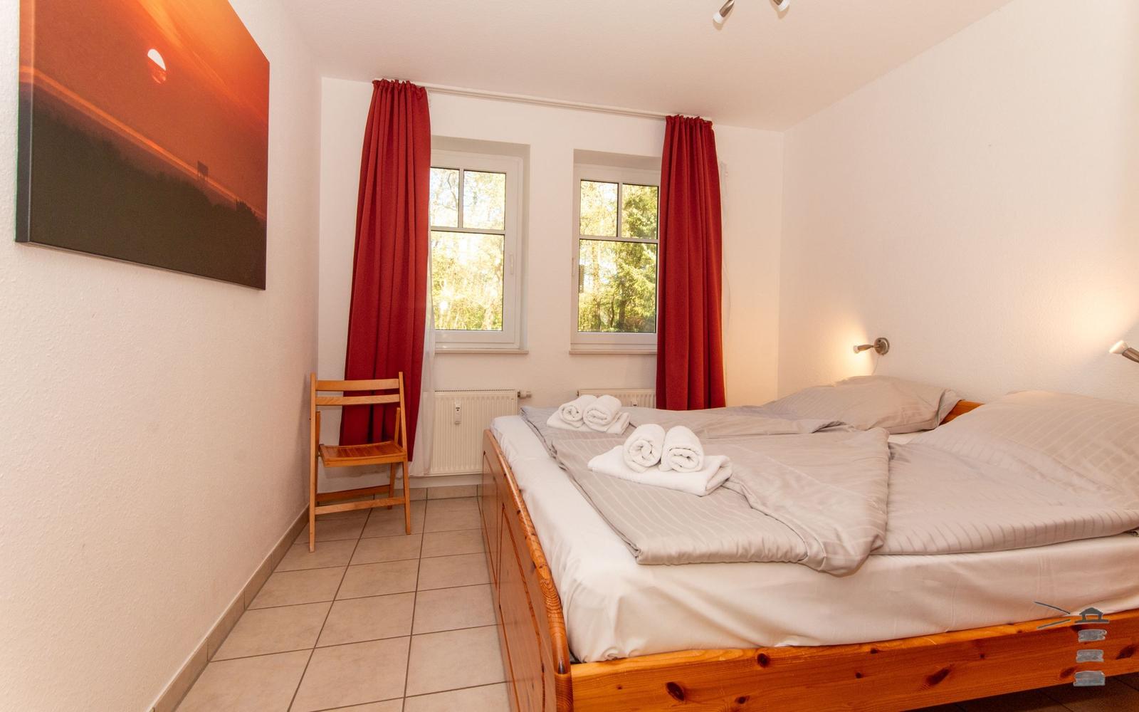 Schlafzimmer mit Doppelbett, roten Vorhängen und Holzstuhl.