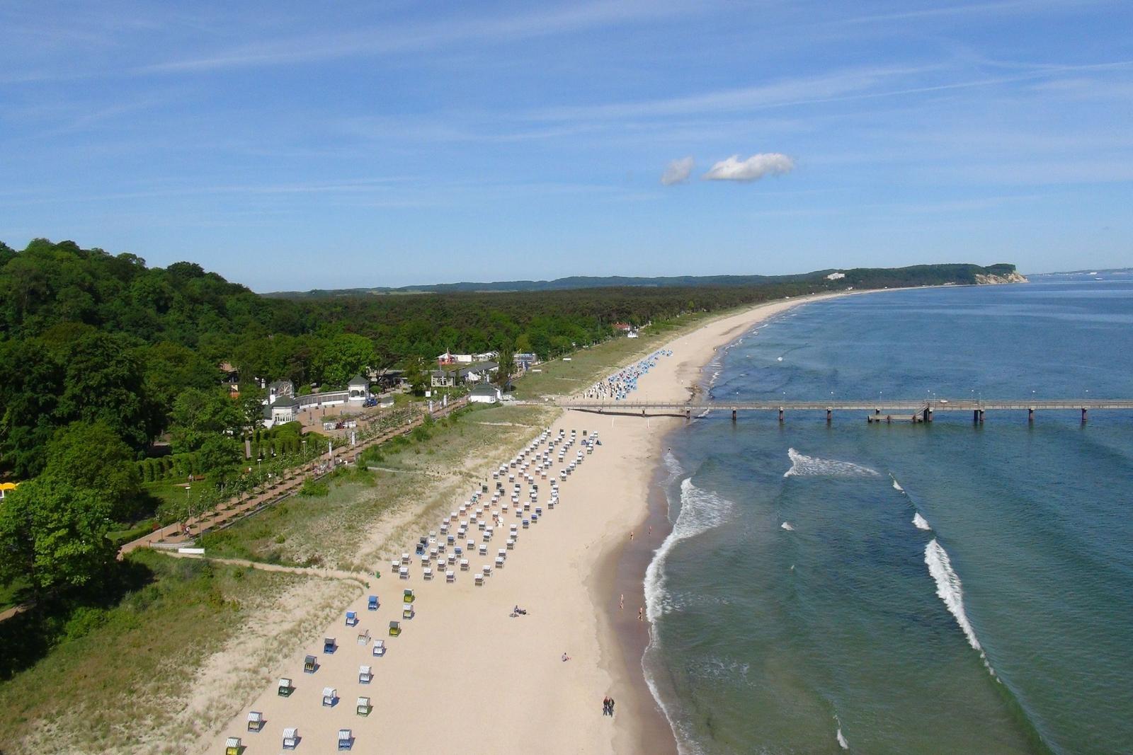 Strand mit Strandkörben, Steg und Wald im Hintergrund.