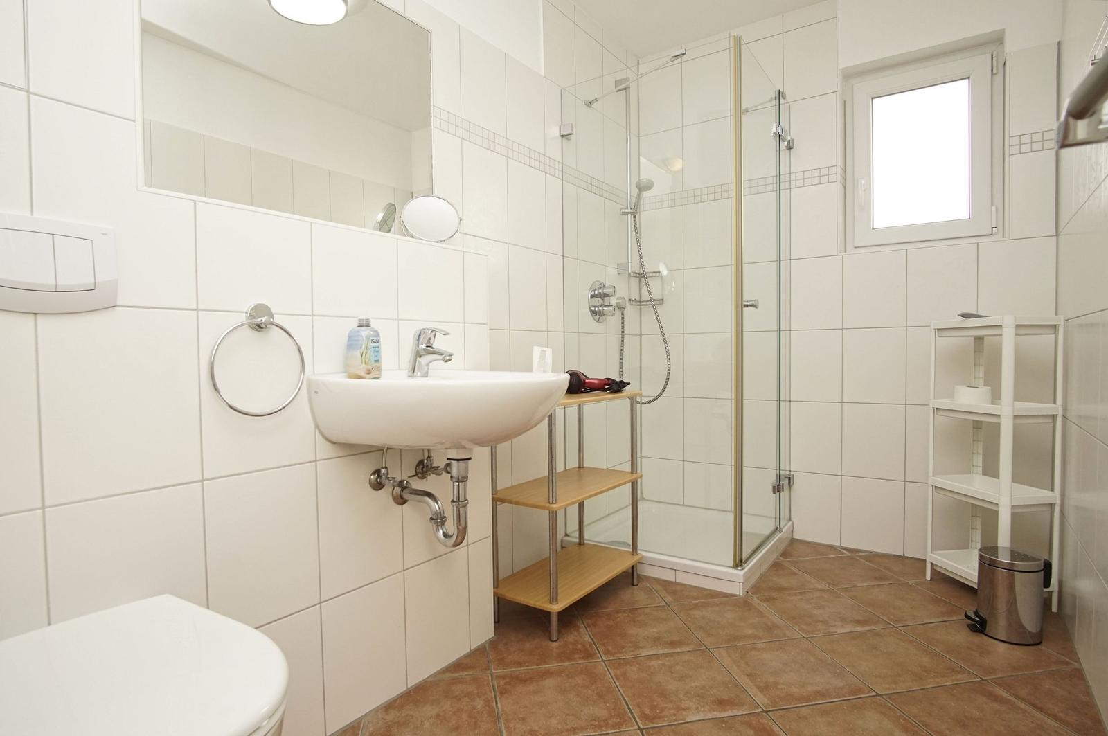 Badezimmer mit Dusche, Waschbecken und Toilette. Fliesenboden und Spiegelschrank.