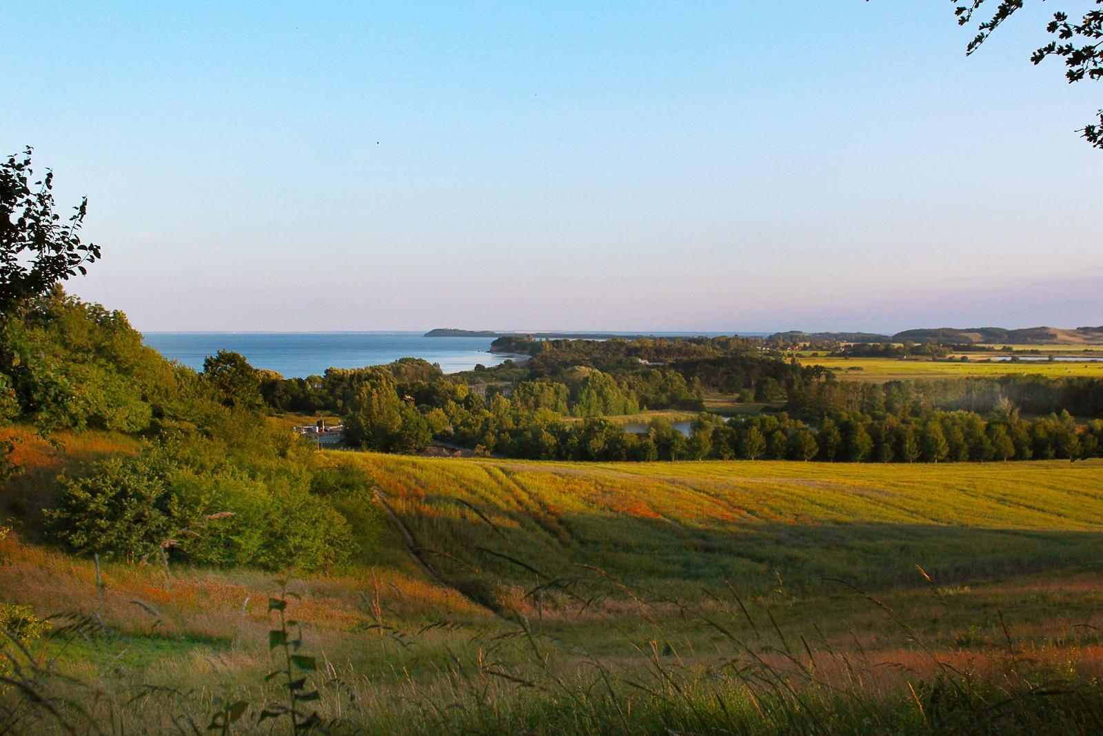 Weitläufige Landschaft mit Feldern, Bäumen und Blick auf einen See.