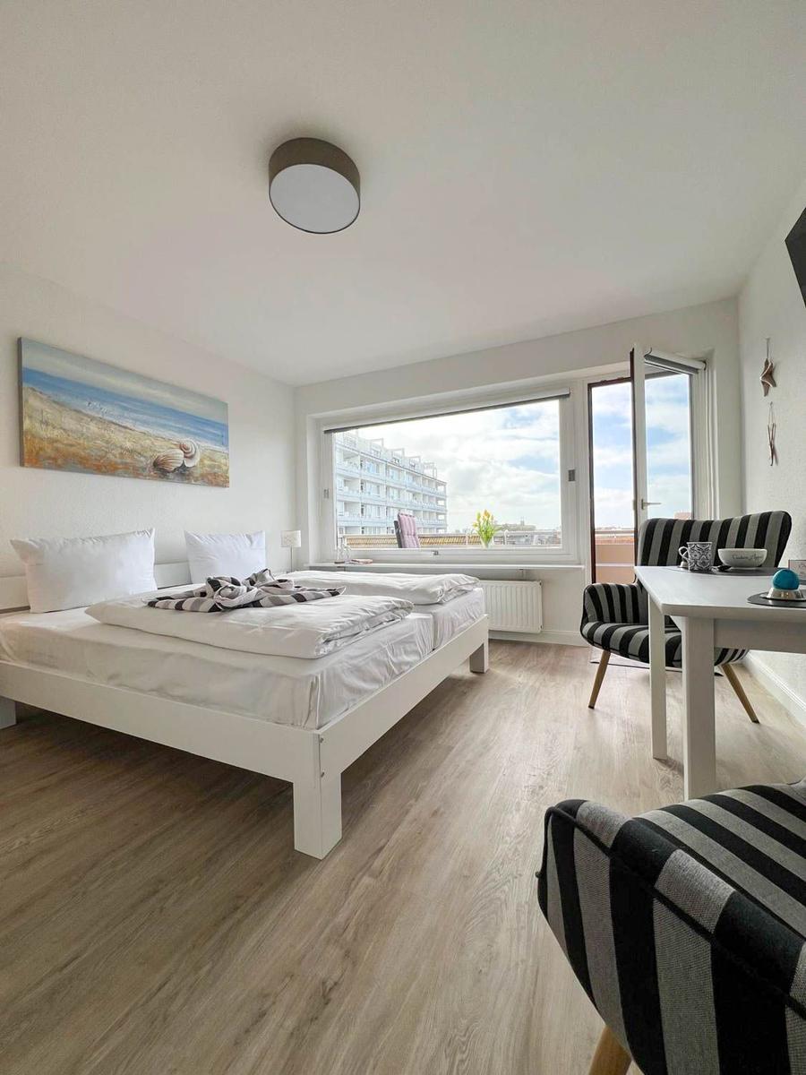Schlafzimmer mit Bett, Tisch und Stühlen. Fenster mit Blick auf Gebäude.