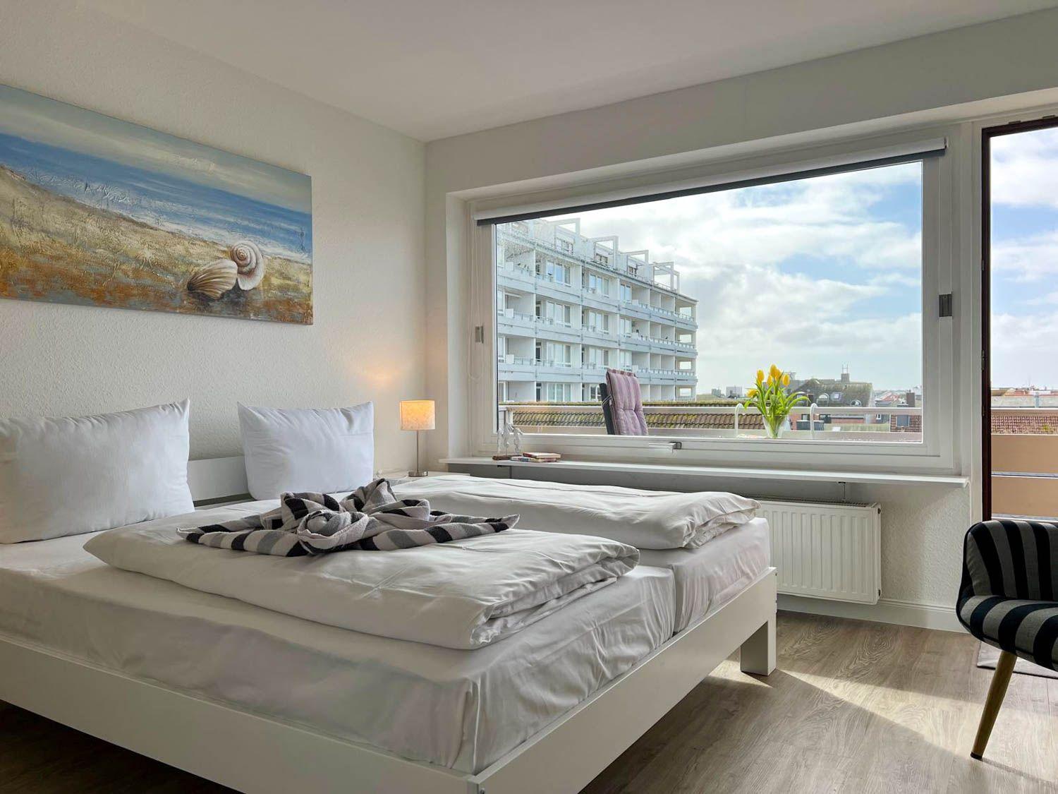 Schlafzimmer mit Bett, Fenster und Blick auf Gebäude.